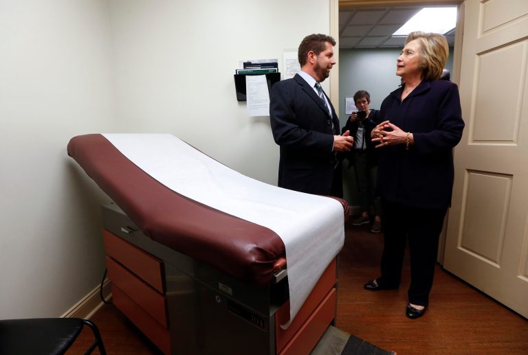 Democratic presidential candidate Hillary Clinton listens to Dr. Christopher Beckett, CEO of Williamson Health and Wellness Center during a tour an exam room of the facility in Williamson, W.Va. With the hourglass running out for his administration, President Barack Obama's health care law is struggling in many parts of the country. Double-digit premium increases and exits by big-name insurers have caused some to wonder whether 