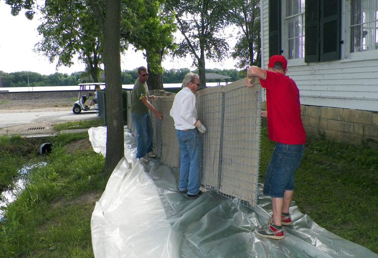 Three generations of the Bankhead family prepare to place a canvass wall around a historic home built in 1850 by their ancestors Wednesday, July 2, 2014, in Clarksville, Mo. Thomas Bankhead, middle, lives in home. His cousin, Reid, left, and his grandson, Alex, right, were lifting up the wall, with plans to later add sand in the middle as protection from the surging Mississippi River a short distance away. (AP Photo/Jim Salter)