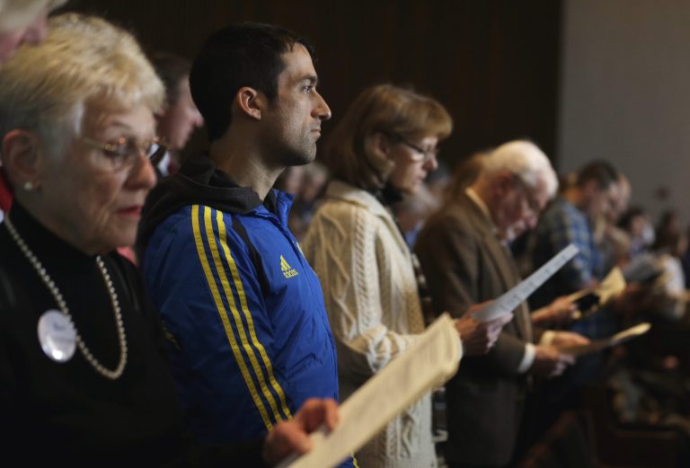 Wearing his Boston Marathon runner's jacket, David Delmar, 28, second from left, a member of Trinity Episcopal Church in Boston, attends a service at Temple Israel, which allowed the Trinity congregation to hold their service, Sunday, April 21, 2013, in Boston. Trinity is within the blocked-off area near the finish line of the Boston Marathon, where earlier in the week two bombs exploded. Delmar, who finished the marathon about 30 minutes before the explosions, was running his first marathon as part of charity to Trinity. (AP Photo/Julio Cortez)