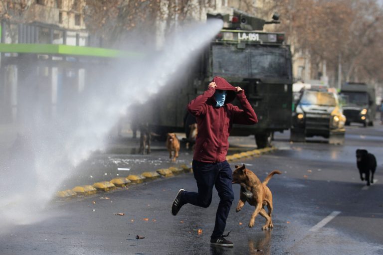 A masked protester runs away from a water cannon, during a student protest in Santiago, Chile, Thursday, August 21, 2014. Tens of thousands of students protested in the third massive march of the year in Chile. The students are unhappy with the pace of education reform that President Michelle Bachelet has been moving forward. (AP Photo / Luis Hidalgo)