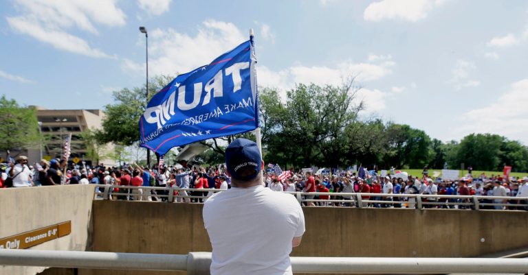 Dustin Marvin, a supporter of President Donald Trump, holds a flag as protestors march through downtown Dallas, Sunday, April 9, 2017. (AP Photo/LM Otero)