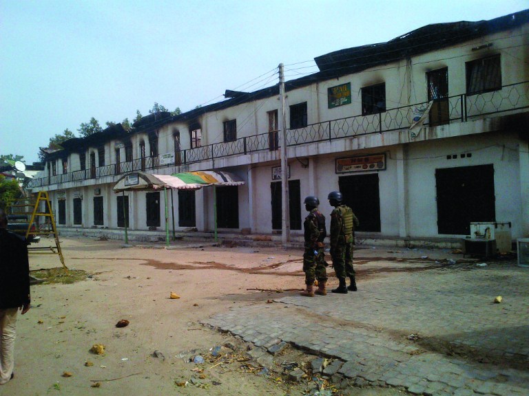 In this photo taken with a mobile phone, soldiers stand outside a burnt out shopping mall in Maiduguri, Nigeria, Monday, Oct. 8, 2012. Nigerian soldiers angry about the killing of an officer razed buildings and shot dead more than 30 civilians Monday in a northeastern city long under siege by a radical Islamist sect. An Associated Press reporter in Maiduguri, the spiritual home of the sect known as Boko Haram, counted the dead while on a tour of the still-smoldering neighborhood. (AP Photo / Abdulkareem Haruna)