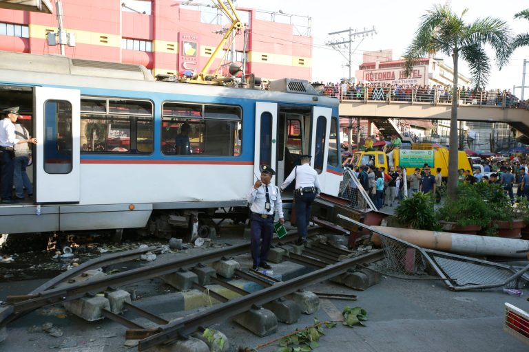 Train guards gather at the site of an elevated commuter train known as Metro Rail Transit or MRT after it overshot its tracks and derailed at the end station Wednesday, Aug. 13, 2014, injuring dozens in suburban Pasay city south of Manila, Philippines. Senior Superintendent Florencio Ortilla, who heads the Pasay city police, said the train toppled concrete posts, spraying debris and damaging cars in the crowded intersection. Hernando Cabrera, spokesman of the agency that operates the train system, said the train had a 