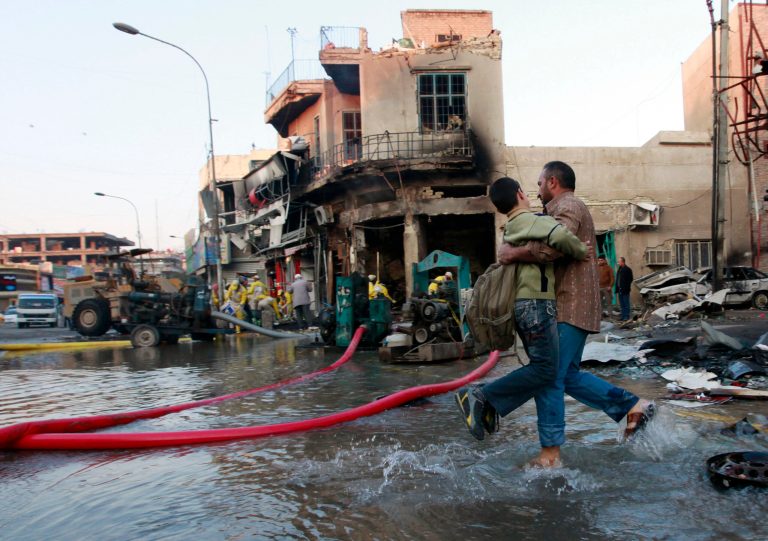 An Iraqi man helps his son who is headed to school at the site of a car bomb attack in Baghdad, Iraq, Tuesday, Feb. 18, 2014. A wave of explosions rocked mainly Shiite neighborhoods in Baghdad shortly after sunset on Monday, killing and wounding scores of people. (AP Photo/Hadi Mizban)