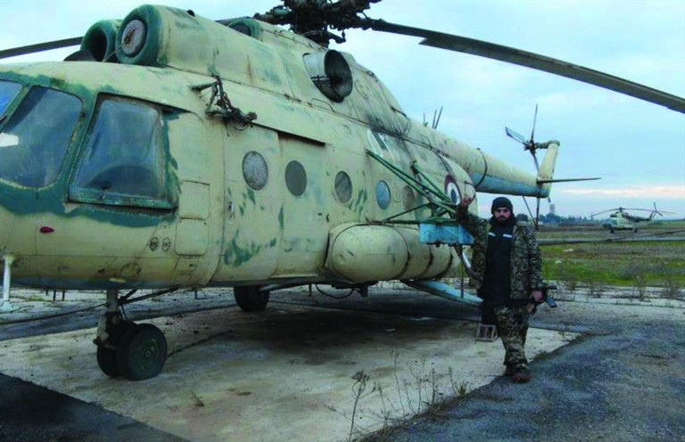 This citizen journalism image provided by Edlib News Network, ENN, which has been authenticated based on its contents and other AP reporting, shows a Syrian rebel posing next to a damaged Syrian air force helicopter, at Taftanaz air base that was captured by rebels, in Idlib province, northern Syria, Friday Jan. 11, 2013. Islamic militants seeking to topple President Bashar Assad took full control of a strategic northwestern air base Friday in a significant blow to government forces, seizing helicopters, tanks and multiple rocket launchers, activists said. (AP Photo/Edlib News Network ENN)