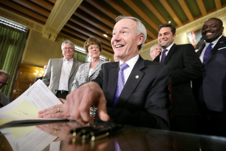 Arkansas Gov. Asa Hutchinson reaches for a pen before finishing a bill signing ceremony at the Arkansas state Capitol in Little Rock, Ark., as legislators watch Monday, April 6, 2015. (AP Photo/Danny Johnston)