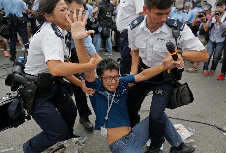 A pro-democracy protester is taken away by police offers as an ambulance tries to leave the compound of the chief executive office in Hong Kong, Friday, Oct. 3, 2014. Hong Kong protesters on Friday welcomed an overnight offer by the territory's leader of talks to defuse the crisis over demonstrations seeking democratic reforms, though they continued to demand he resign and maintained barricades around government headquarters, frustrating staff going to work. (AP Photo/Vincent Yu)