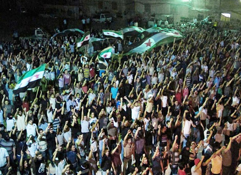   In this citizen journalism image made and provided by the Kfar Suseh Coordinating of the Syrian Revolution, on Tuesday, June 12, 2012, anti-Syrian regime protesters raise up their hands and wave revolutionary flags during a demonstration at Kfar Suseh area, in Damascus, Syria. Syria has accused the U.S. of 