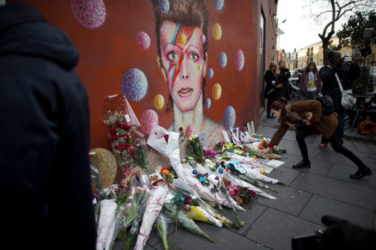 A woman lays flowers next to a mural of British singer David Bowie by artist Jimmy C in Brixton, south London. Bowie was born in Brixton. (AP Photo/Matt Dunham)