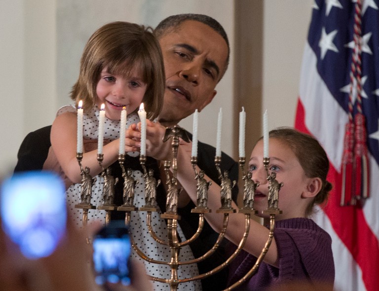 President Barack Obama holds up Kylie Schmitter as she and her sister Lainey Schmitter, lights the menorah during the first of two Hanukkah receptions in the Grand Foyer of the White House in Washington, Thursday, Dec. 5, 2013. The Schmitter girls attended the reception with their mother Drew Schmitter and their father Jacob could not attend because he is deployed in Afghanistan. (AP Photo/Carolyn Kaster)