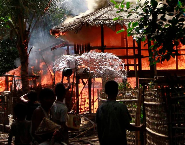   A person throws a bucket of warter at a house engulfed in flames in Sittwe, Myanmar, Monday, June 11, 2012. With fearful residents cowering indoors, security forces patrolling a tense town in western Myanmar collected bodies Monday from the debris of homes burned down over the weekend in some of the country's deadliest sectarian bloodshed in years. The Buddhist-Muslim violence, which has left at least seven people dead and hundreds of homes torched since Friday, poses one the biggest tests yet for Myanmar's new government as it struggles to reform the nation after generations of military rule. (AP Photo/Kihn Maung Win)  