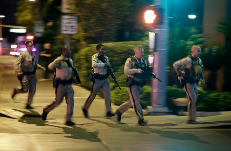 Police run to cover at the scene of a shooting near the Mandalay Bay resort and casino on the Las Vegas Strip, Sunday, Oct. 1, 2017, in Las Vegas. Multiple victims were being transported to hospitals after a shooting late Sunday at a music festival on the Las Vegas Strip. (AP Photo/John Locher)