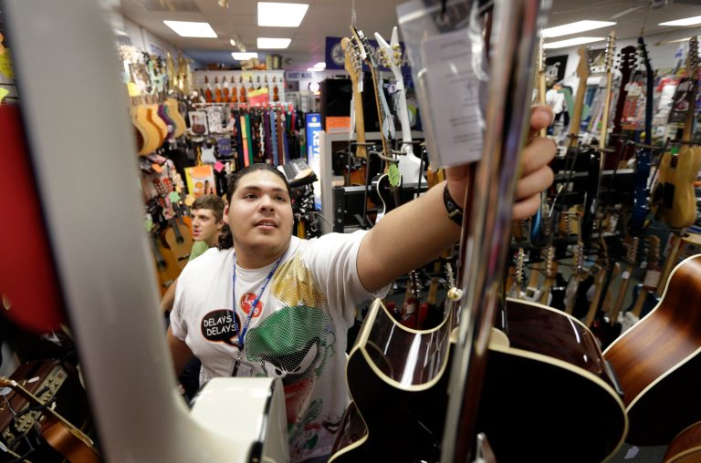 In this Tuesday, Sept. 24, 2013 photo Kevin Sandoval, of Chelsea, Mass., places a guitar on a rack after trying the instrument out at a music store, in Lowell, Mass. The government reports how much U.S. businesses adjusted their stockpiles in September on Wednesday, Nov. 20, 2013. (AP Photo/Steven Senne)