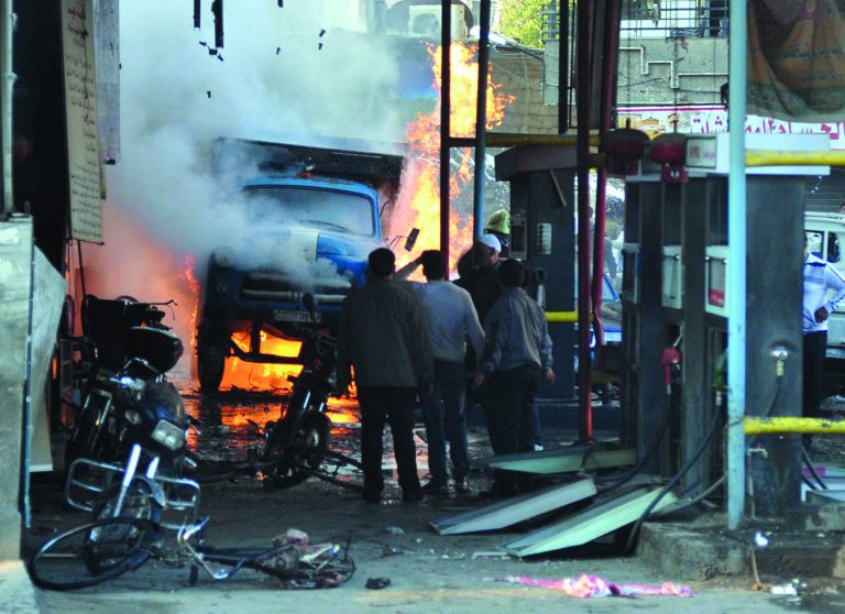 In this photo released by the Syrian official news agency SANA, Syrian citizens stand near a burning truck that was destroyed by two cars bombs, at Jaramana neighborhood, in the suburb of Damascus, Syria, Wednesday, Nov. 28, 2012. (AP Photo/SANA)