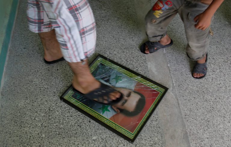 A Syrian man breaks a photo of the Syrian president Bashar Assad that was on  wall in a classroom in a school where they took refuge from the fighting, in the town of Kafr Hamra, some ten kilometers (six miles) north of the center of  Aleppo city, Syria, Tuesday, Aug. 7, 2012. (AP Photo/ Khalil Hamra)