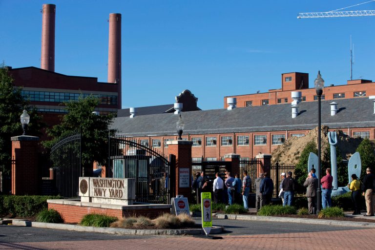 FILE - In this Sept. 18, 2013 file photo, employees of the Washington Navy Yard line up to enter through a gate two days after a gunman killed twelve people and was killed himself inside.  Officials are renaming the Washington Navy Yard building where a gunman fatally shot 12 people in September before he was killed by police. Navy Vice Adm. William Hilarides said in an email to employees on Tuesday that Building 197 will be named after Joshua Humphreys, who designed the Navy's first six frigates. Hilarides said officials are also 