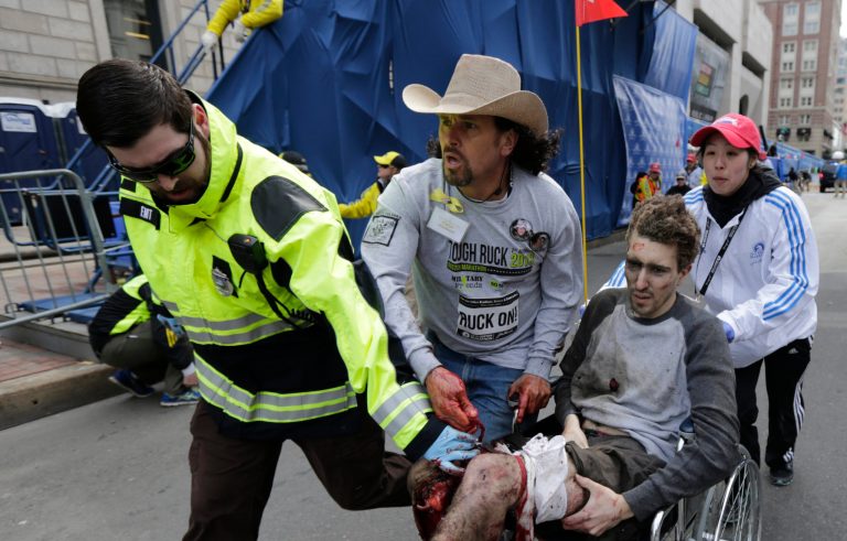 FILE - In this April 15, 2013 file photo, an emergency responder and volunteers, including Carlos Arredondo in the cowboy hat, push Jeff Bauman in a wheel chair after he was injured in an explosion near the finish line of the Boston Marathon Monday, April 15, 2013 in Boston.   Arredondo and Bauman are among the guests who will sit with first lady Michelle Obama Tuesday when President Barack Obama delivers the annual State of the Union address.   (AP Photo/Charles Krupa, File)