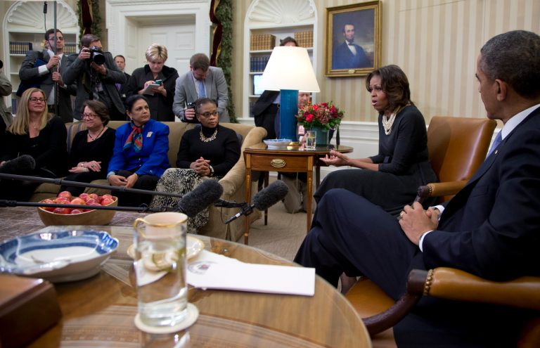 First lady Michelle Obama speaks to the media as President Barack Obama sits right, as they meet with a group of mothers in the Oval Office of the White House in Washington, Wednesday, Dec. 18, 2013, to discuss how health care reform could benefit their families. (AP Photo/Carolyn Kaster)