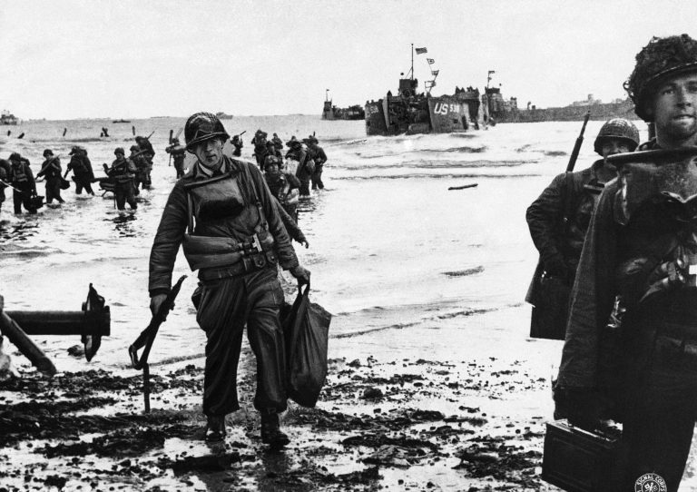 U.S. assault troops, laden with equipment, wade through the surf to a Normandy beach from landing craft in June 1944 to support those who had gone before in the D-Day assault. (AP Photo)