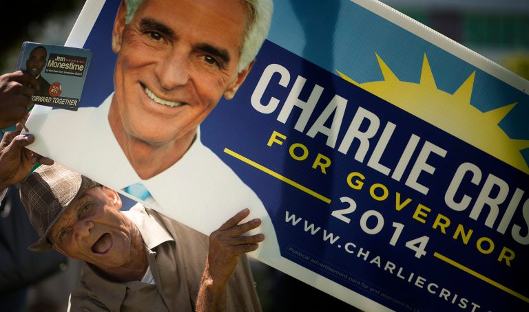 A campaign supporter displays a sign as former Republican Gov. Charlie Crist makes a campaign stop Sunday, Aug. 24, 2014, in North Miami, Fla., as Crist tries to get his old job back as a Democrat. He is spending the weekend campaigning in the Democratic base of South Florida. He's seeking to drive up support for Tuesday's primary. (AP Photo/J Pat Carter)