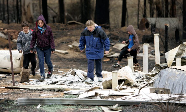 FILE - In this Feb. 8, 2009 file photo twelve-year-old Rebecca Goudge, second from right, and neighbors nine-year-olds Dean, left, and Kirk Mercuri, right, and their sister Alison, 11, walk around the wreckage of Goudge's home in Kinglake, northeast of Melbourne, Australia. The fire, which killed 119 people, was the largest of a series of blazes that tore through the southern Australian state of Victoria in 2009, leaving 173 people dead and destroying more than 2,000 homes in just over a single day. Survivors of one of Australia's deadliest wildfires are expected to be awarded nearly 500 million Australian dollars ($470 million) in a class action settlement reached on Tuesday, July 15, 2014, the largest such compensation in the nation's history. (AP Photo/Rick Rycroft, File)