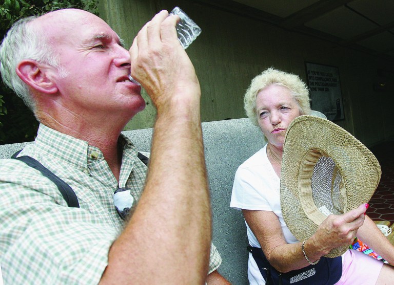 A couple sip water to combat the heat as they wait for a Metro train at the Arlington Cemetery station. This summer, Metro has regularly allowed riders to drink water on the transit system during heat waves. (Examiner file photo)