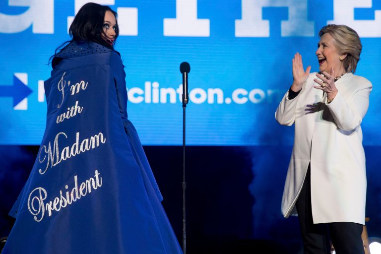 Democratic presidential candidate Hillary Clinton applauds on stage as artist Katy Perry arrives with a cape that reads 