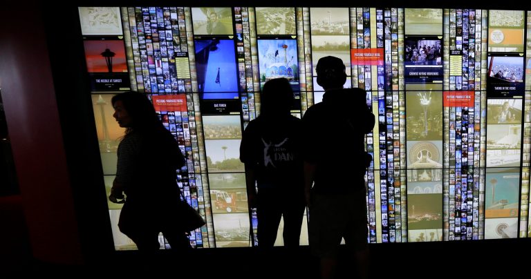 In this photo taken Sept. 19, 2014, visitors to the Space Needle in Seattle interact with a large touch-screen photo display wall that lets visitors see historical photos as well as photos shared by other visitors. The display as well as a new tablet and mobile phone app are adding to the allure of one of Seattle's top tourist destinations. (AP Photo/Ted S. Warren)
