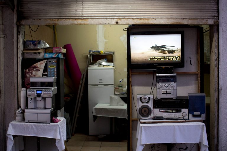 In this Sunday, July 13, 2014 photo, a TV screen shows the ongoing fighting between Israel and Gaza at the entrance to a coffee shop in downtown Tel Aviv, Israel. Israelis are struggling to decide whether to carry on with their routines or take emergency precautions. (AP Photo/Oded Balilty)