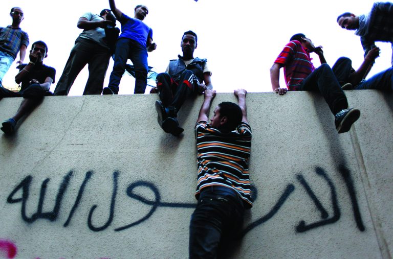 Egyptian protesters climb the walls of the U.S. embassy with Arabic graffiti that reads 