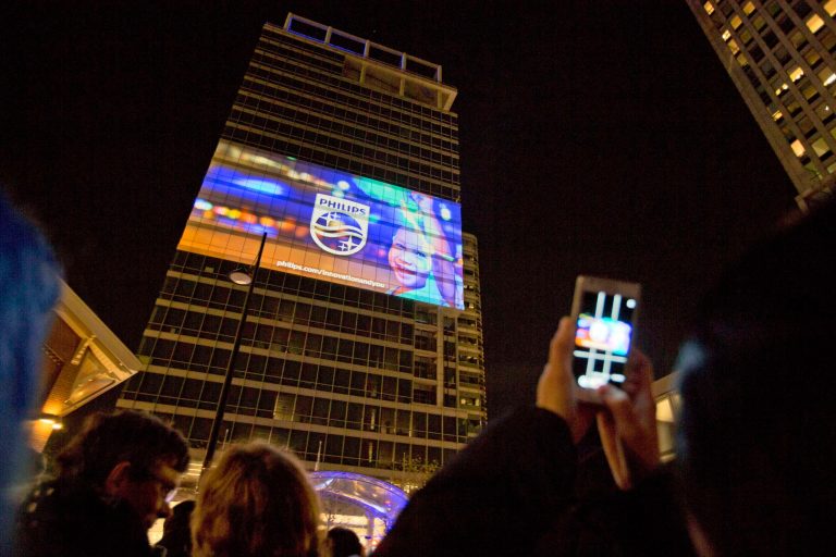 FILE - In this Nov. 13, 2013 file photo, spectators take photos as they watch the new company logo and branding campaign of Royal Philips NV projected onto the Philips headquarters in Amsterdam, Netherlands. The campaign portrays Philips as an innovation company. Royal Philips NV has reported a return to profitability in the fourth quarter, with operating profits up in all its main businesses: lighting, consumer appliances and health care equipment. The company Tuesday reported net profit of 409 million euros (usd 559 million), compared to a loss of 423 million euros in the same period a year earlier when it was fined 509 million euros for price-fixing in the TV market. Fourth quarter sales rose 0.6 percent to 6.80 billion euros, which Philips would have been a 7 percent rise comparing like-for-like businesses and stripping currency effects. (AP Photo/Peter Dejong, File)