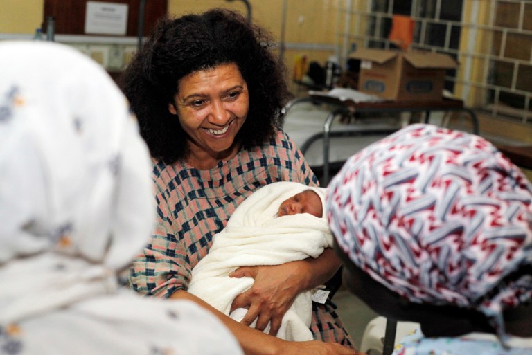 In this photo taken July 24, 2013 Michelle Faul, the veteran foreign correspondent named by The Associated Press to head its bureau in Lagos, Nigeria, with the newborn baby of Naimot Alabi , right, at Island Maternity Hospital while reporting on progress in child birth and maternal health care in the country. Faul, 57, joined the AP in her native Zimbabwe in 1983 and has reported for the news cooperative from bases in South Africa, Puerto Rico, Kenya and Ivory Coast. (AP Photo.Sunday Alamba)