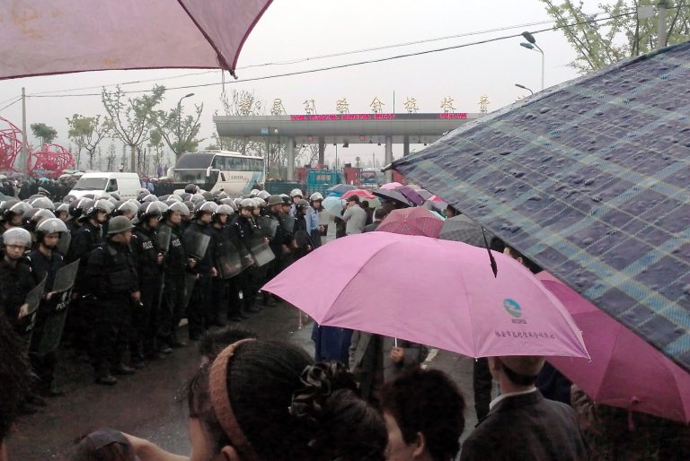 In this Sunday, May 11, 2014 photo released by Hong, Chinese police with shields stand guard near the toll of a highway during a protest against the construction of a waste incinerator in Yuhang district, Hangzhou in China's Zhejiang province. Government pledges to seek public approval for a planned waste incinerator in eastern China failed to appease the project's neighbors Monday, May 12, 2014 after thousands of them, concerned over potential health hazards, blocked the highway and clashed with police in a bid to stop the construction. (AP Photo/Hong)