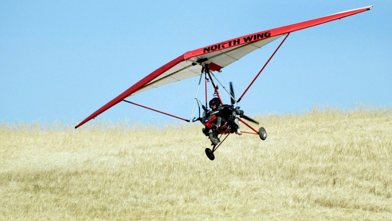 An unidentified pilot and his passenger fly in an ultralight aircraft low to the ground during drills.