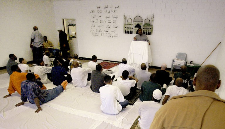 As Imam Menelik Muhammad stands beside a Quranic prayer on a wall facing Mecca, he begins Friday afternoon's worship as late arrivers enter the room used as an Islamic mosque at a prison.