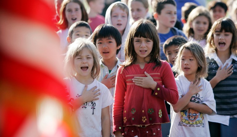 School students recite the Pledge of Allegiance during a school assembly. 