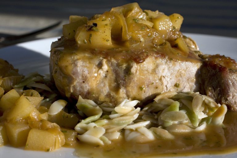 In this photo, a dish of pork chops with pear, caramelized onions, and rosemary is displayed.