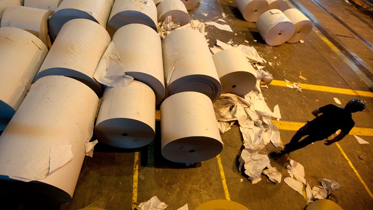 A worker walks past paper rolls at a newsprint plant.