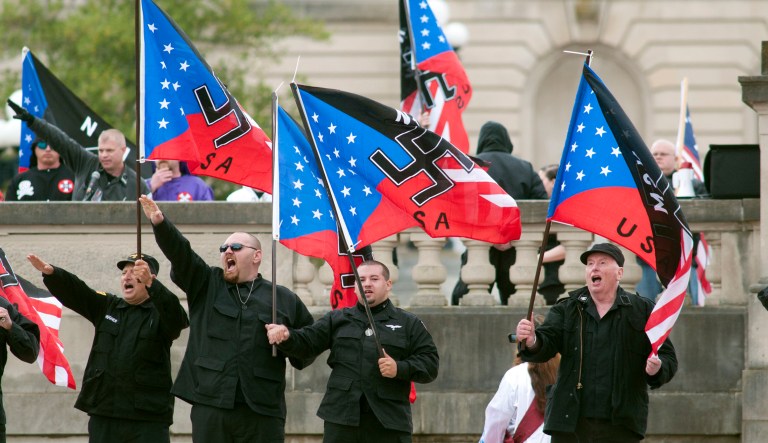 Members of the National Socialists Movement and the White Knights of the Klu Klux Klan salute during a rally Saturday April 21, 2012, at the Capitol in Frankfort, Ky. At least 70 law enforcement officers were present to control a crowd of 150 to 200 demonstrators when a group of neo-Nazis and Ku Klux Klan members rallied against illegal immigration on the steps of the Kentucky Capitol.