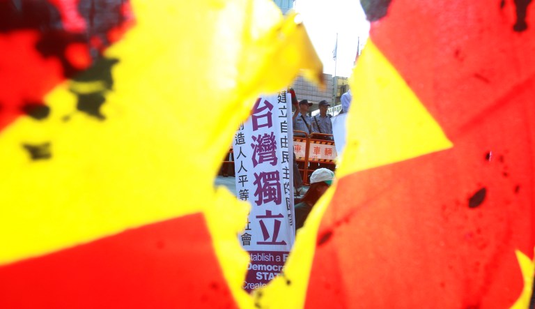 A protester holds a slogan reading ''Taiwan Independence'' is seen through a burned China national flag outside of the meeting place of the Taipei-Shanghai forum in Taipei on Aug. 23, 2016.