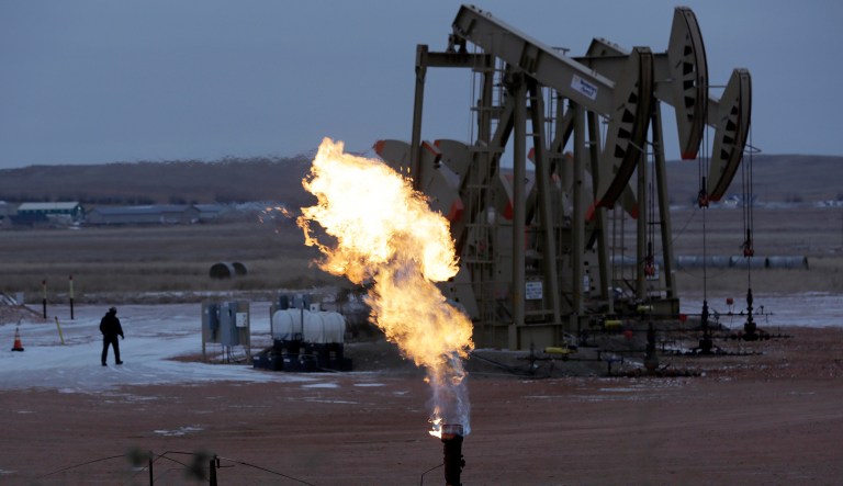 Workers tend to oil pump jacks behind a natural gas flare near Watford City, N.D., on Oct. 22, 2015.