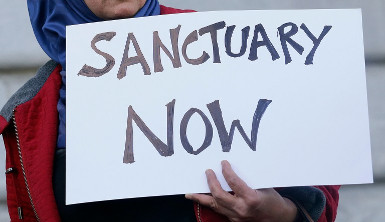 A pro-sanctuary city sign is shown.