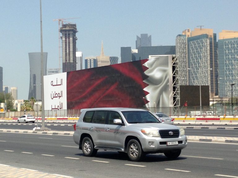 In this 2017 photo, an SUV drives past a billboard featuring the Qatari flag and the slogan "God, Nation, Emir" in Doha, Qatar.