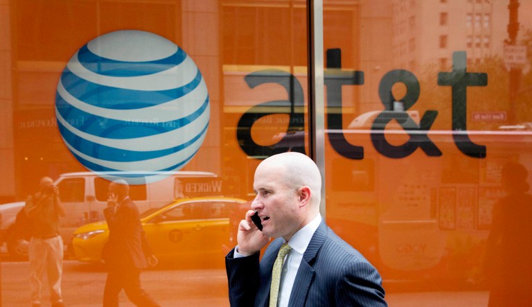 A man using a mobile phone walks past an AT&T store.