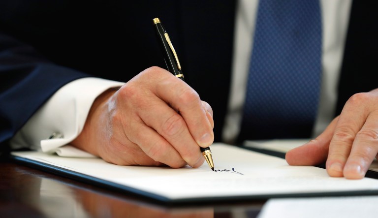 President Trump signs something in the White House in Washington.