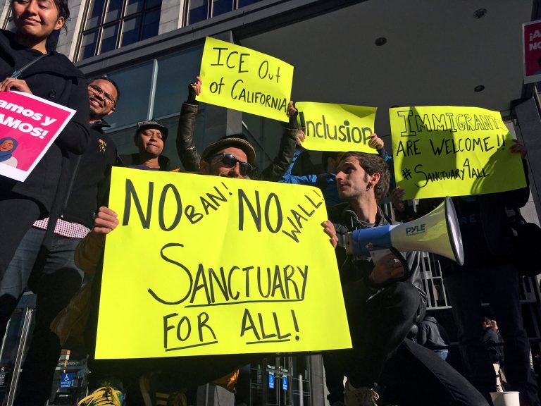  this April 14, 2017, file photo, protesters hold up signs outside a courthouse where a federal judge was to hear arguments in the first lawsuit challenging President Donald Trump's executive order to withhold funding from communities that limit cooperation with immigration authorities in San Francisco.