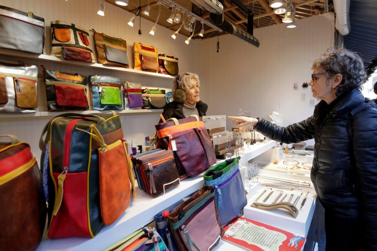 In this Thursday, Dec. 7, 2017, photo, Tanya Carol-Lugones helps a shopper in her booth featuring Viva Zapata bags and Caracruz jewelry, at the Union Square Holiday Market in New York. At the holiday markets that pop up annually, many of the booths are staffed by artisans hoping to make a significant portion of their revenue or to get visibility that will translate into sales other times of the year. 
