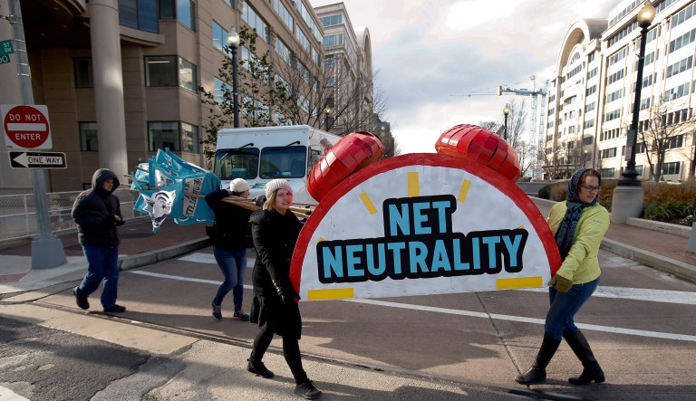 Sammi LeMaster, left, and Katherine Fuchs, right, carry the top of an alarm clock display that reads "Net Neutrality."