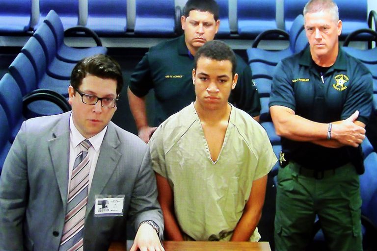 Zachary Cruz, center, the brother of Florida school shooting suspect Nikolas Cruz, is displayed in a monitor via closed circuit television from the main jail as he as he makes his first appearance on charges of trespassing on the grounds of Marjory Stoneman Douglas High School, Tuesday, March 20, 2018, at the Broward County Courthouse in Fort Lauderdale, Fla.