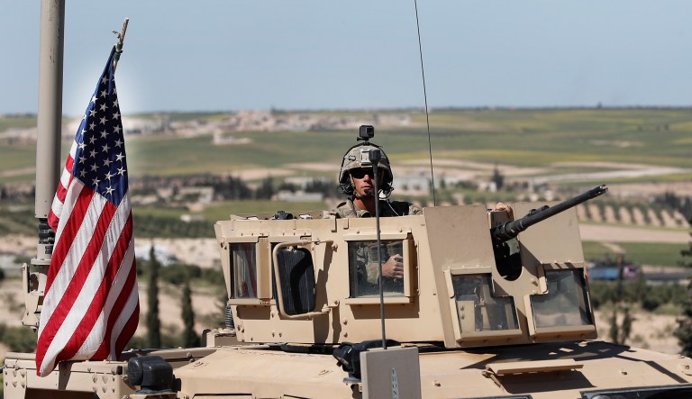 A U.S. soldier sits in an armored vehicle on a road leading to the tense front line with Turkish-backed fighters, in Manbij, north Syria, Wednesday, April 4, 2018. President Donald Trump expects to decide "very quickly" whether to remove U.S. troops from war-torn Syria, saying their primary mission was to defeat the Islamic State group and "we've almost completed that task." 
